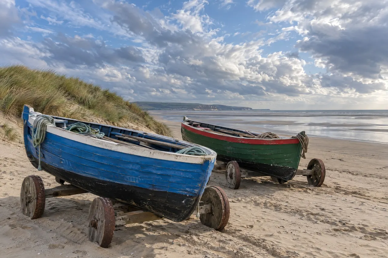 Deux flobarts peints en bleu et en vert, sur leurs chariots à roues de bois, au pied de la dune