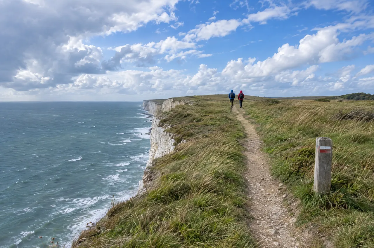 Le sentier sur le haut de la falaise de craie du Blanc-Nez, un poteau balisé blanc et rouge et deux marcheurs au loin